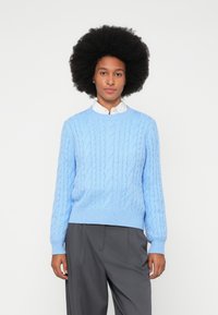 Vaaleansininen neulottu kaapelineulepaita pyöreällä pääntiellä ja ribbireunoilla. Yhdistetty harmaisiin housuihin, joissa on rakennekuvio.