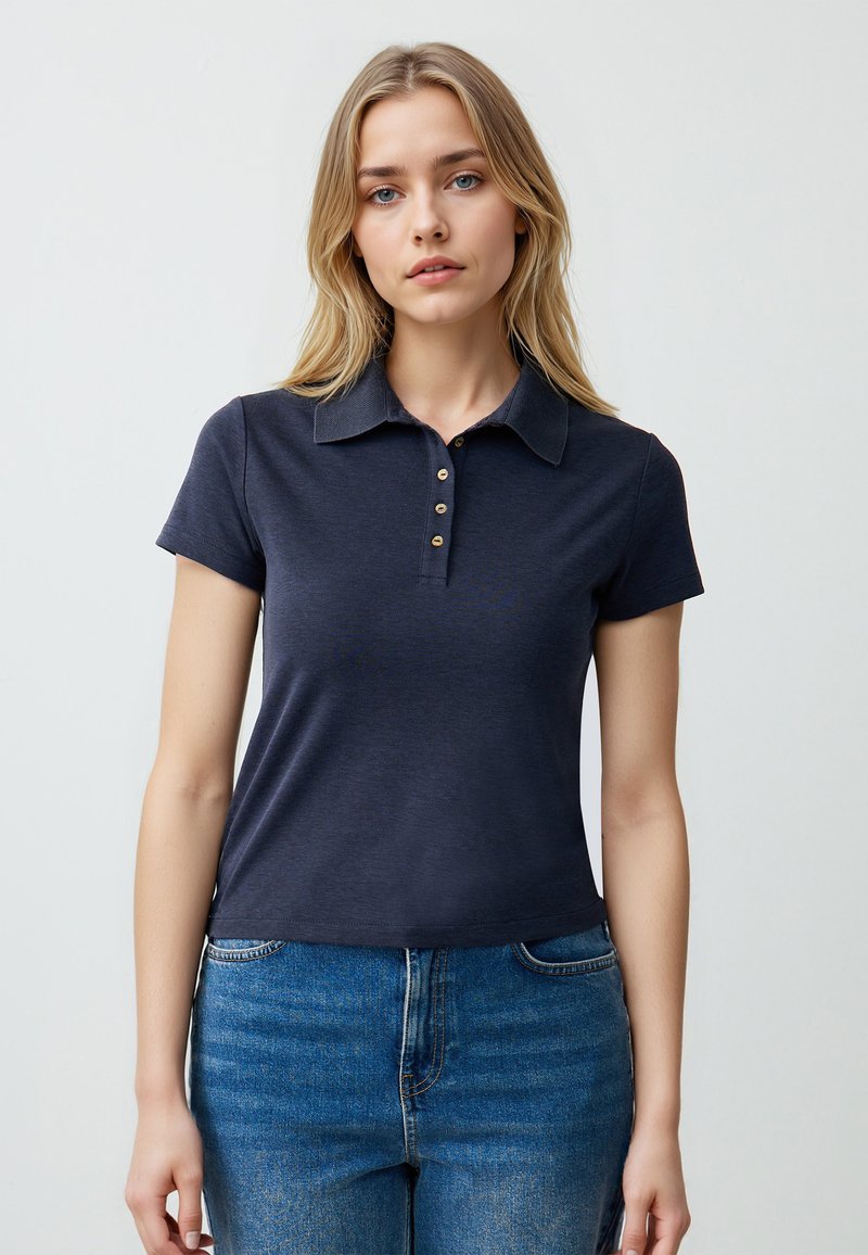 Polo in blu navy con maniche corte, apertura a bottoni con bottoni dorati e colletto. Realizzato in un tessuto morbido e liscio.