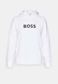 Sweat à capuche blanc en tissu doux, avec un grand logo noir "BOSS" sur le devant. Épaules tombantes et ourlet côtelé.