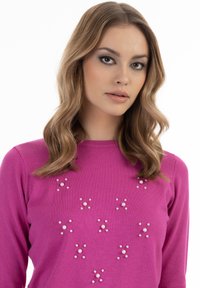 Maglione rosa con scollatura rotonda, adornato con decorazioni di perle di diverse dimensioni disposte in un motivo a stella sulla parte anteriore.