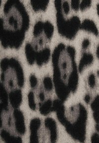Nahaufnahme von weichem Stoff mit unregelmäßigen Leopardflecken in Schwarz und Dunkelgrau auf einem hellgrauen Hintergrund.