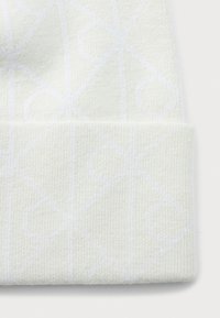 Witte gebreide muts met een subtiel geometrisch patroon van cirkels en lijnen, omgevouwen aan de onderrand op een effen achtergrond.