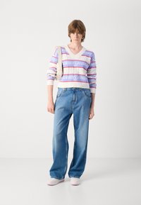 Witte trui met roze en lavendel strepen en "tommy jeans" tekst, gecombineerd met losse blauwe denim jeans. Platte schoenen met roze accenten.