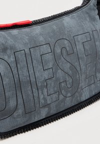 Grå teksturert tøyveske med store "DIESEL" bokstaver, svarte detaljer og en rød stropp langs toppen.