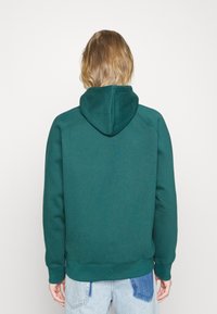 Felpa con cappuccio verde dal tessuto morbido, maniche raglan e tasca a marsupio. Le finiture a costine su polsini e orlo garantiscono una vestibilità aderente. Jeans in denim taglia oversize.