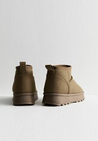 Bruine suède enkellaarsjes met een ronde neus, korte schacht, trekriem en textuurrubber zool, weergegeven vanaf de achterkant.