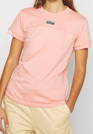 Różowy bawełniany t-shirt z krótkimi rękawami, z czarną łatką z logo na klatce piersiowej i białymi paskami na rękawach. Gładka faktura, dopasowany krój.