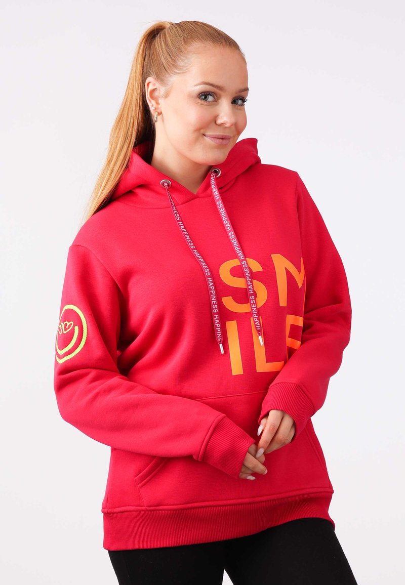 Felpa rossa con la scritta "SMILE" stampata in arancione, dotata di tasca frontale e lacci regolabili. Accentuata con un logo a faccina sorridente sul maniche.