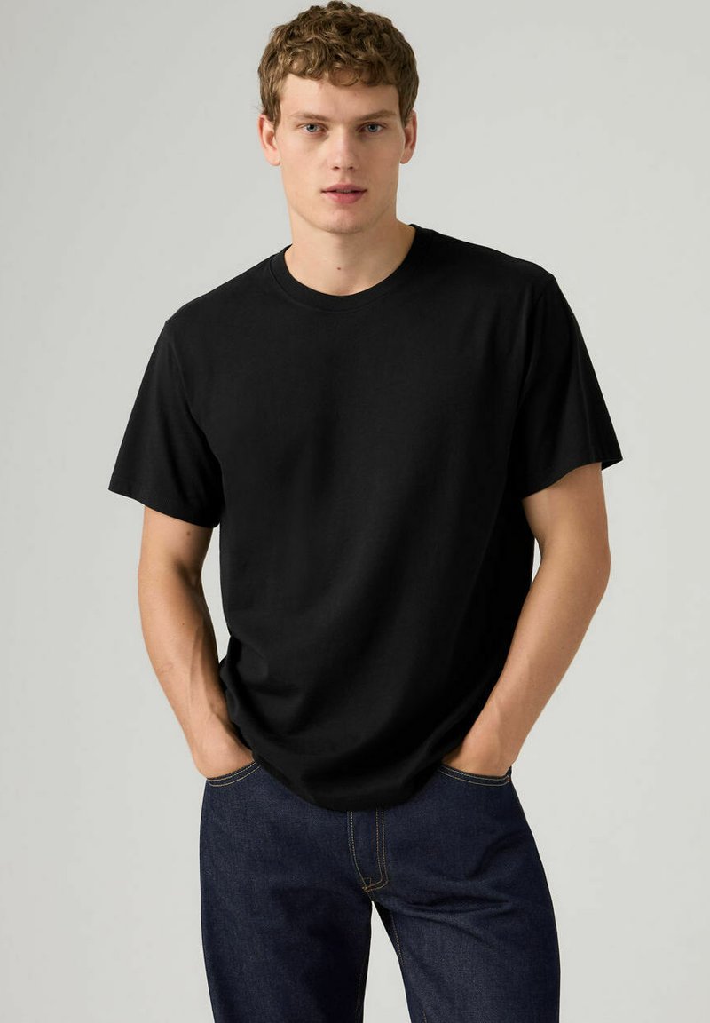 T-shirt nera in cotone con scollo rotondo, maniche corte e vestibilità comoda, abbinata a jeans di denim blu. Design semplice, senza motivi.