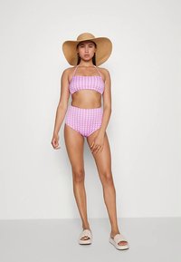 Conjunto de biquíni rosa e branco em vichy, com top bandeau, parte de baixo de cintura alta e chapéu de palha, complementado por sandálias bege sem calcanhar.
