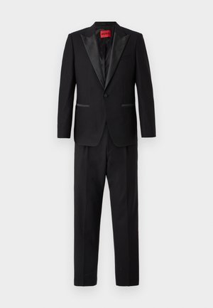 Costume noir avec une veste texturée à revers en satin et deux poches avant, associée à un pantalon assorti. Étiquette HUGO visible à l'intérieur.