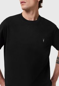 T-shirt nero a maniche corte in cotone. Presenta un colletto rotondo e un piccolo design ricamato sul petto sinistro. Tessuto liscio.