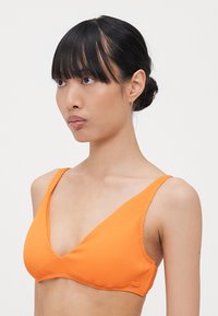 Haut de bikini orange à côtes avec un design en V, des bretelles larges et une texture douce. Remarquable pour sa couleur vive et ses détails matériels minimalistes.