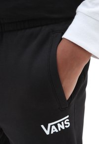 Pantaloni sportivi neri con tasche laterali, realizzati in misto cotone. Presentano un logo Vans bianco vicino alla tasca, una texture liscia e una vita elastica.