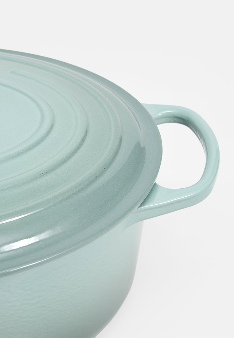 Gietijzeren pan met een lichtblauwe buitenkant en glanzende afwerking. Het deksel heeft concentrische groeven en een zijkant-handgreep voor gemakkelijk tillen.