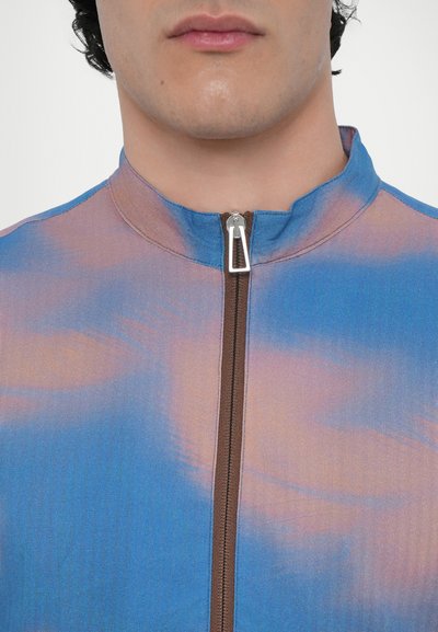 Blue and pink gradient zip-up jacket with a high collar, featuring a contrasting brown zipper and smooth, textured fabric.