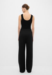 Zwarte geribbelde tanktop gecombineerd met zwarte wijde geplooide broek. De outfit heeft een naadloos ontwerp en een aansluitende tailleband.