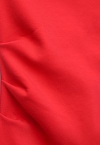 Czerwona elastyczna tkanina o gładkiej teksturze, z miękkimi fałdami i jednolitym wzorem powierzchni. Idealna do zastosowania w odzieży.