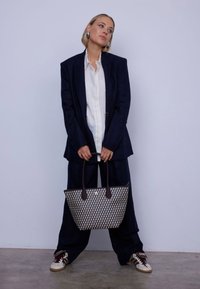 Sac en jute tissé bleu marine et crème avec des poignées en cuir brun foncé. Le sac présente un motif géométrique et un design ouvert.