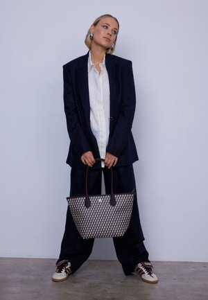 Gewebte Tragetasche in Marineblau und Creme mit dunkelbraunen Ledergriffen. Die Tasche verfügt über ein geometrisches Muster und ein offenes Design.