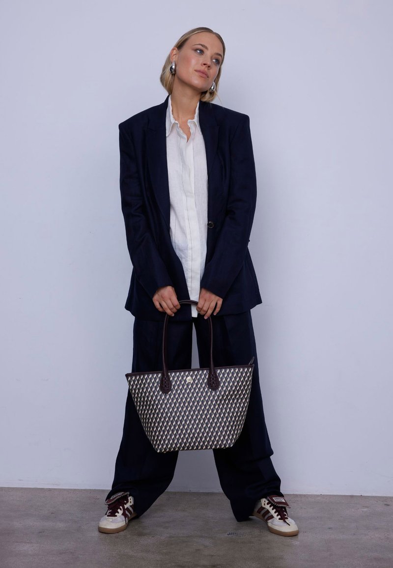 Sac en jute tissé bleu marine et crème avec des poignées en cuir brun foncé. Le sac présente un motif géométrique et un design ouvert.