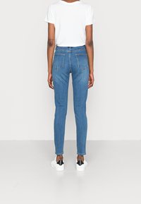 Úzké modré džíny s vysokým pasem, které mají dvě zadní kapsy, spárované s bílými botami a volným bílým tričkem.