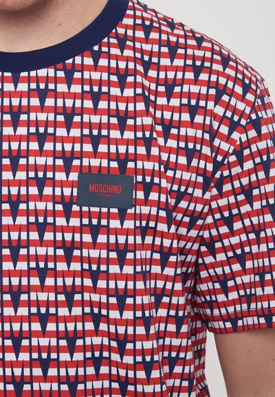 T-shirt a maniche corte in rosso, bianco e blu navy con motivo geometrico, caratterizzato da un piccolo etichetta Moschino Swim sul petto. Materiale in cotone leggero.