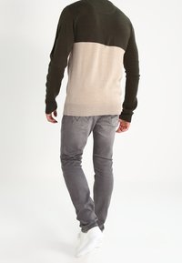 Stickad tröja med en grön överdel och en beige underdel, parat med ljusgrå jeans och vita sneakers.