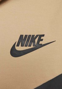 Logotipo da Nike em preto sobre tecido bege, apresentando uma textura suave e um realce curvado abaixo da escrita.