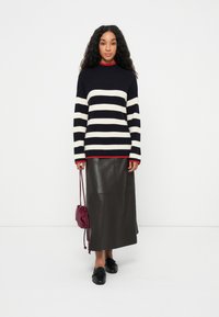 Marinblå och vit randig sweater med röd krage, i kombination med en lång mörkgrön läderkjol och svarta skor, kompletterad av en burfandi väska.