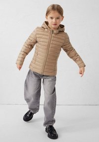 Beige donsjack met capuchon, ritssluiting en horizontaal doorgestikt patroon. Gecombineerd met losse grijze spijkerbroek en zwarte schoenen.