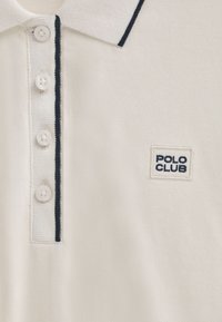 Polo in cotone bianco, con tessuto testurizzato, colletto rifinito in blu navy e quattro bottoni con logo "POLO CLUB" ricamato.