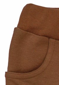 Zbliżenie na kieszeń brązowych spodni z tkaniny z prążkowanym elastycznym paskiem w talii i widocznym przeszyciem.