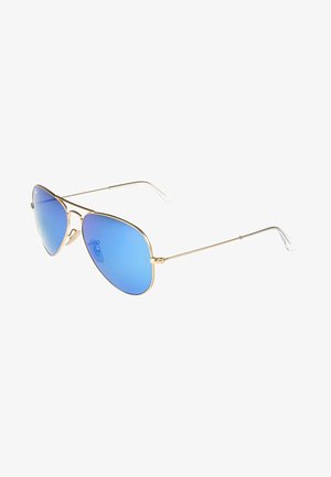 Gafas de sol aviador doradas con lentes degradados azules, montura de metal delgada y puntas de plástico transparente en las patillas. Diseño clásico con una marca sutil.