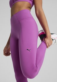 Leggings violet cu talie înaltă, având o textură fină, cu un design elegant și un mic logo Puma negru pe piciorul stâng.