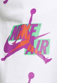 Grafika Nike Air s fialovou a oranžovou siluetou skákající postavy na bílém pozadí s zeleným a fialovým textem.