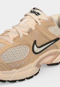 Μπεζ και εκρού αθλητικό παπούτσι Nike με πλέγματα, επενδύσεις από σουέτ, λευκά κορδόνια και λευκό λογότυπο Nike swoosh με μαύρο περίγραμμα.