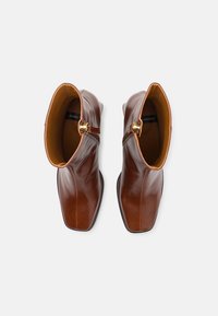 Paire de bottines en cuir brun avec bouts carrés et boucles latérales dorées, vues de dessus sur un fond clair.