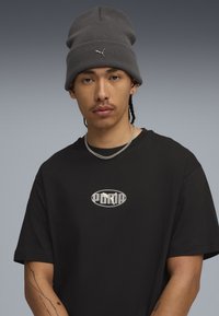 Gray knitted beanie with a small logo, paired with a black short-sleeve t-shirt featuring a reflective oval logo on the chest.