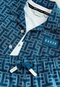 Niebieski zestaw koszula i szorty z geometrycznym wzorem oraz białymi metkami "Baker by Ted Baker", w połączeniu z białą podkoszulką częściowo z widocznym tekstem.