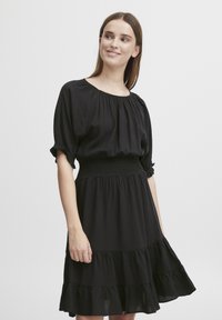 Čierne šaty vyrobené z ľahkej tkaniny, s gumičkovým pásom, krátkymi nariasenými rukávmi a tierovaným volánovým lemom. Jednoduchý, elegantný dizajn.
