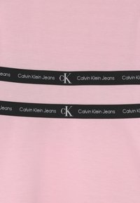 Różowa bluzka z materiału z czarnym pasem w talii z logo "Calvin Klein Jeans" oraz emblematem "CK". Gładka tekstura, casualowy design, dopasowany fason.