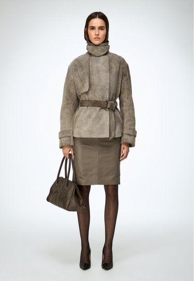 Barna színű velúr dzseki magas gallérral és öves derékkal, összehangolva egy testhezálló olívazöld szoknyával, fekete harisnyával és barna texturált kézitáskával.