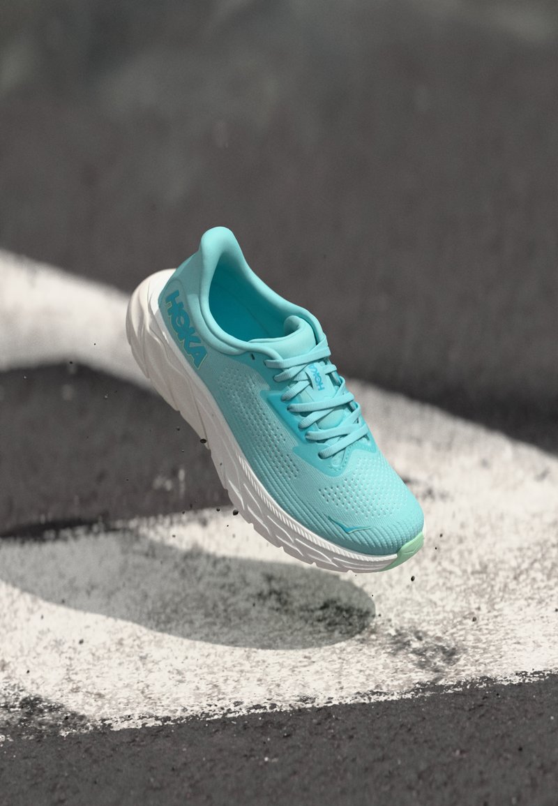 Light blue running shoe with textured mesh upper, cushioned sole, and white accents. Features a rounded shape and lacing system.