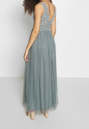 Lange, vloeiende jurk in gedempte teal. Heeft een kralenbezet bustier en een diepgaand V-halsontwerp aan de achterkant. Gemaakt van lichtgewicht tule stof.
