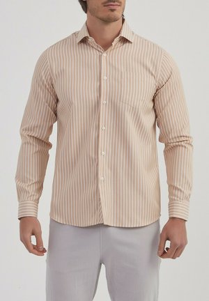 Chemise beige clair avec des rayures verticales blanches, manches longues, col boutonné, poche poitrine unique et texture de tissu lisse.