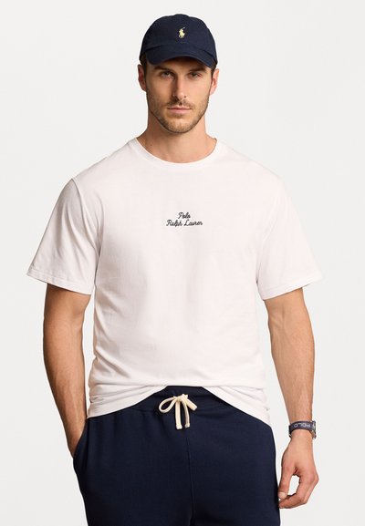 Biała bawełniana koszulka z haftowanym logo "Polo Ralph Lauren", w połączeniu z granatowymi spodniami dresowymi z wiązanym pasem. Noszona pod granatową czapką.