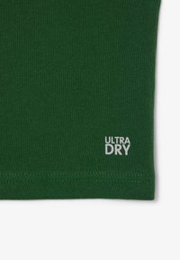 Tissu en coton vert avec une texture lisse et un détail de couture. "ULTRA DRY" imprimé en blanc en bas à droite.