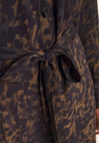 Hnědá a černá látka s leopardím vzorem, se svázaným pasem a zapínáním na knoflík. Měkká textura a splývavý design s volným střihem.