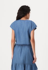 Jeanskjole med tettsittende midje, korte ermer og lagdelt skjørt. Har en ensfarget lyseblå farge og mykt, lett materiale.